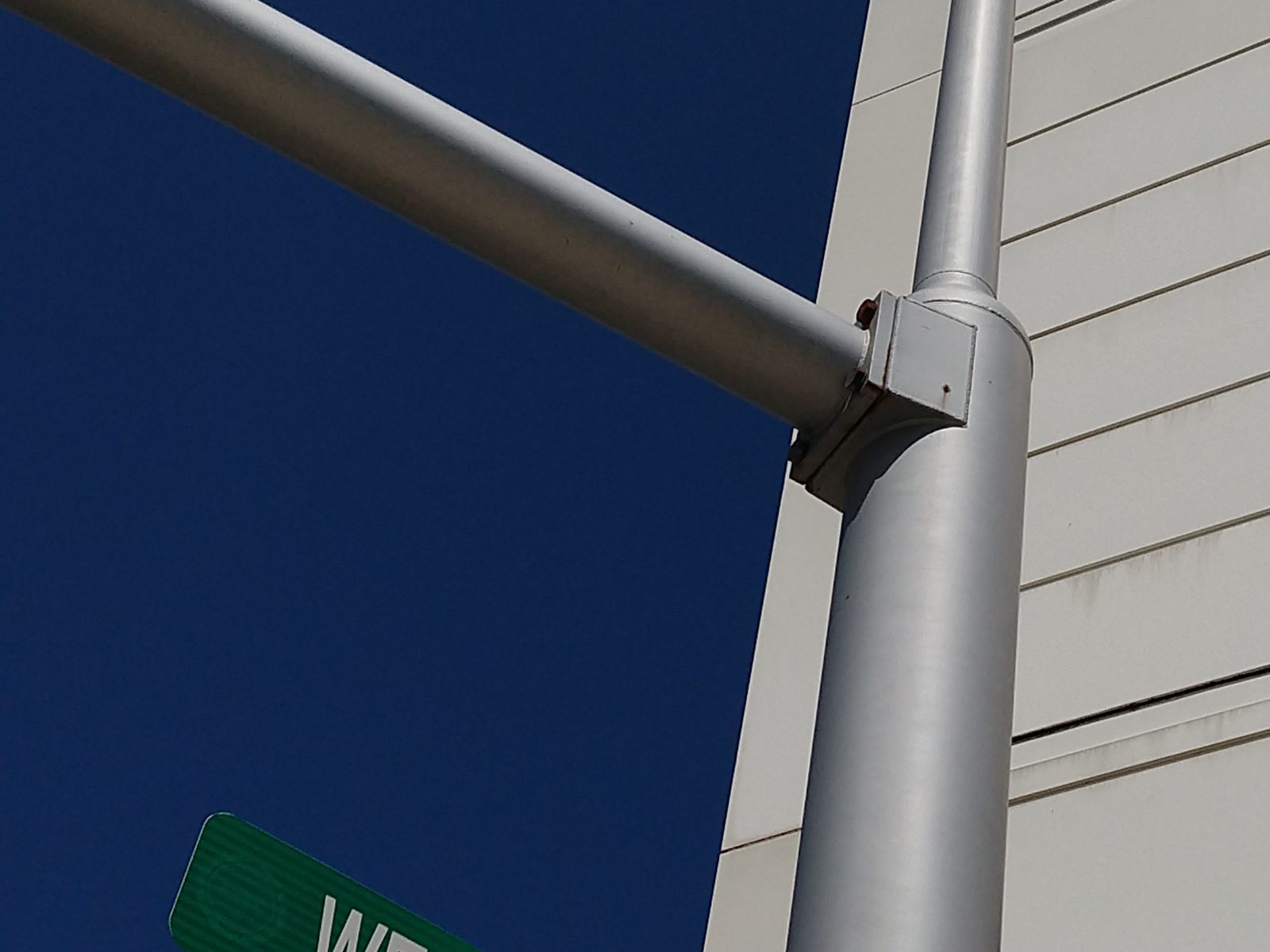 Close-up photograph of the joint where the horizontal mast arm meets the vertical pole, showing a small rectangular bracket and bolted flange rather than any deep embedment