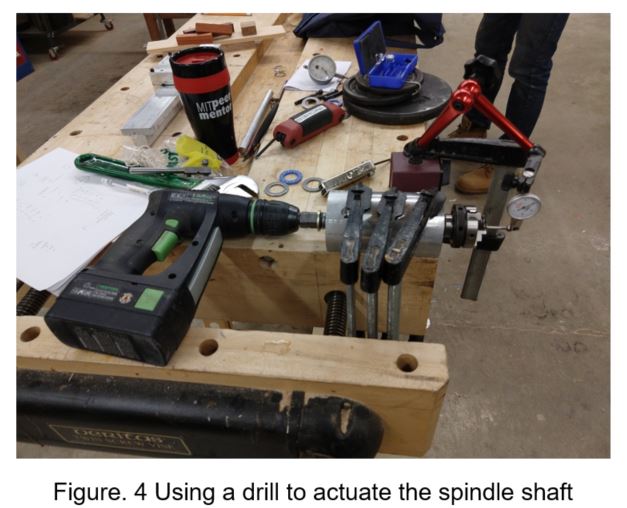 Using a cordless drill to actuate the spindle shaft, with the spindle clamped to the workbench and the dial indicator set up against the chuck
