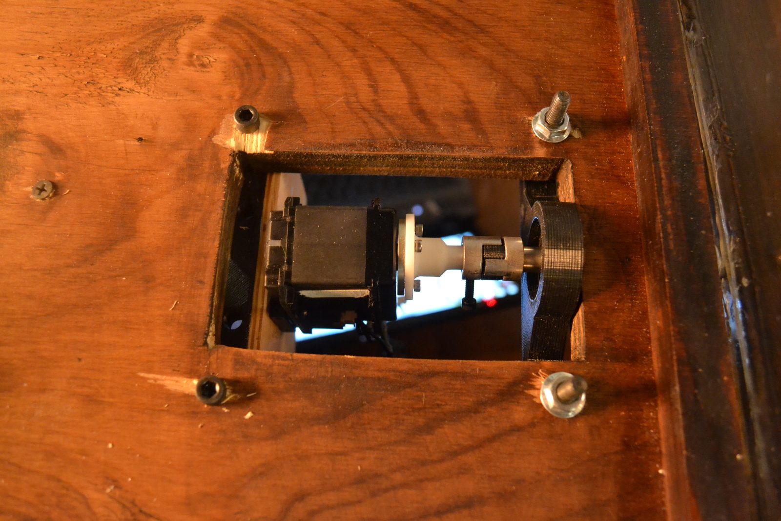 The drive: a stepper motor and flexible shaft coupler mounted inside the desk pedestal, seen through a service cutout in the wood
