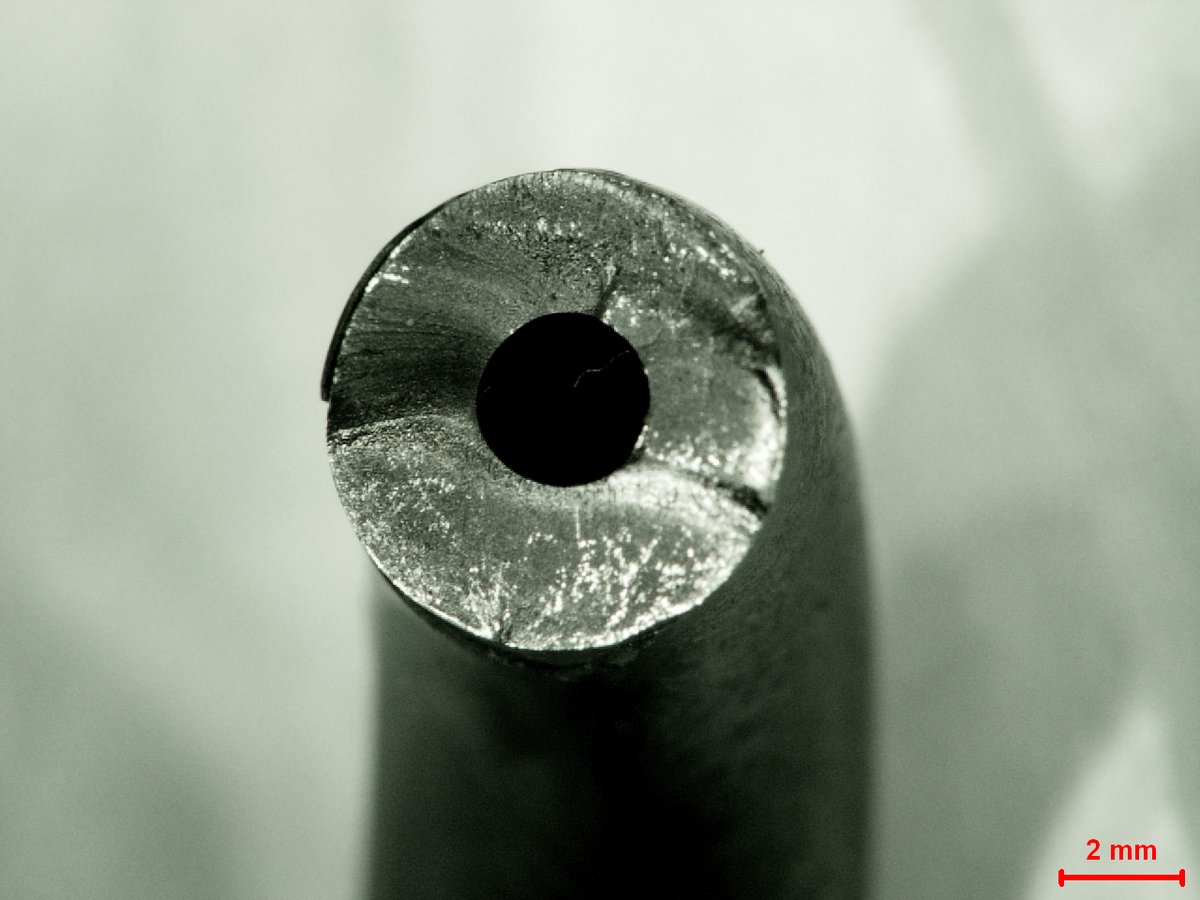 Macro photograph of the fractured end of a fuel line, showing the bore and the fracture surface around it, with a 2 mm scale bar