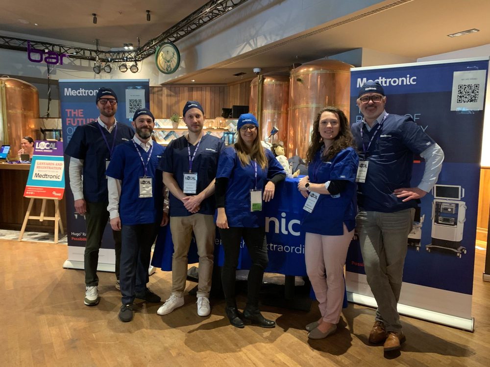 Six colleagues in Medtronic scrubs and beanies at a booth in front of Medtronic banners at the Munich SWE event