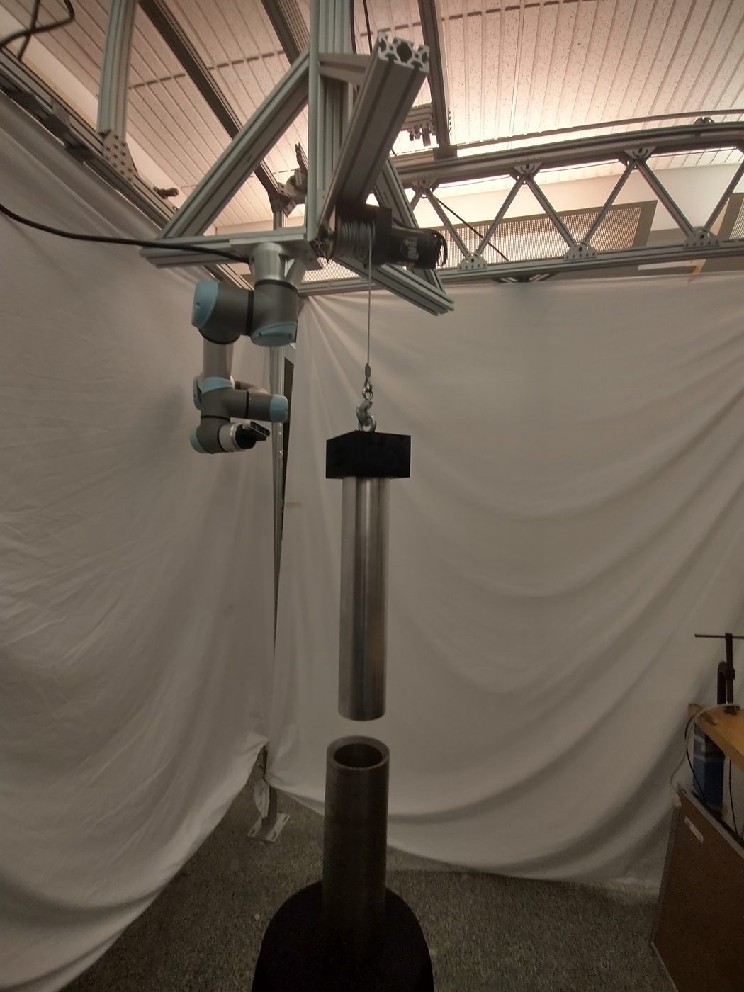 The UR arm hanging upside down from the new girder beside a winch cable holding the aluminium peg above the hole