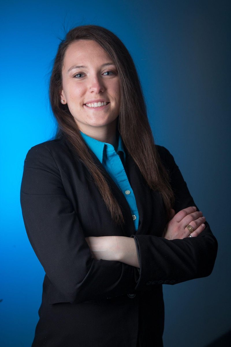 Professional portrait: me in a black blazer and turquoise shirt, arms crossed and smiling, against a blue studio backdrop