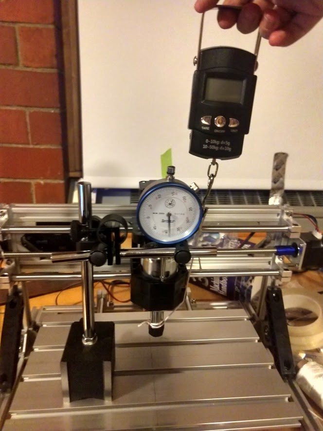 Stiffness test in Z: the luggage scale lifting the collet straight up, with the dial indicator mounted on the Y platform reading the top of the spindle bracket