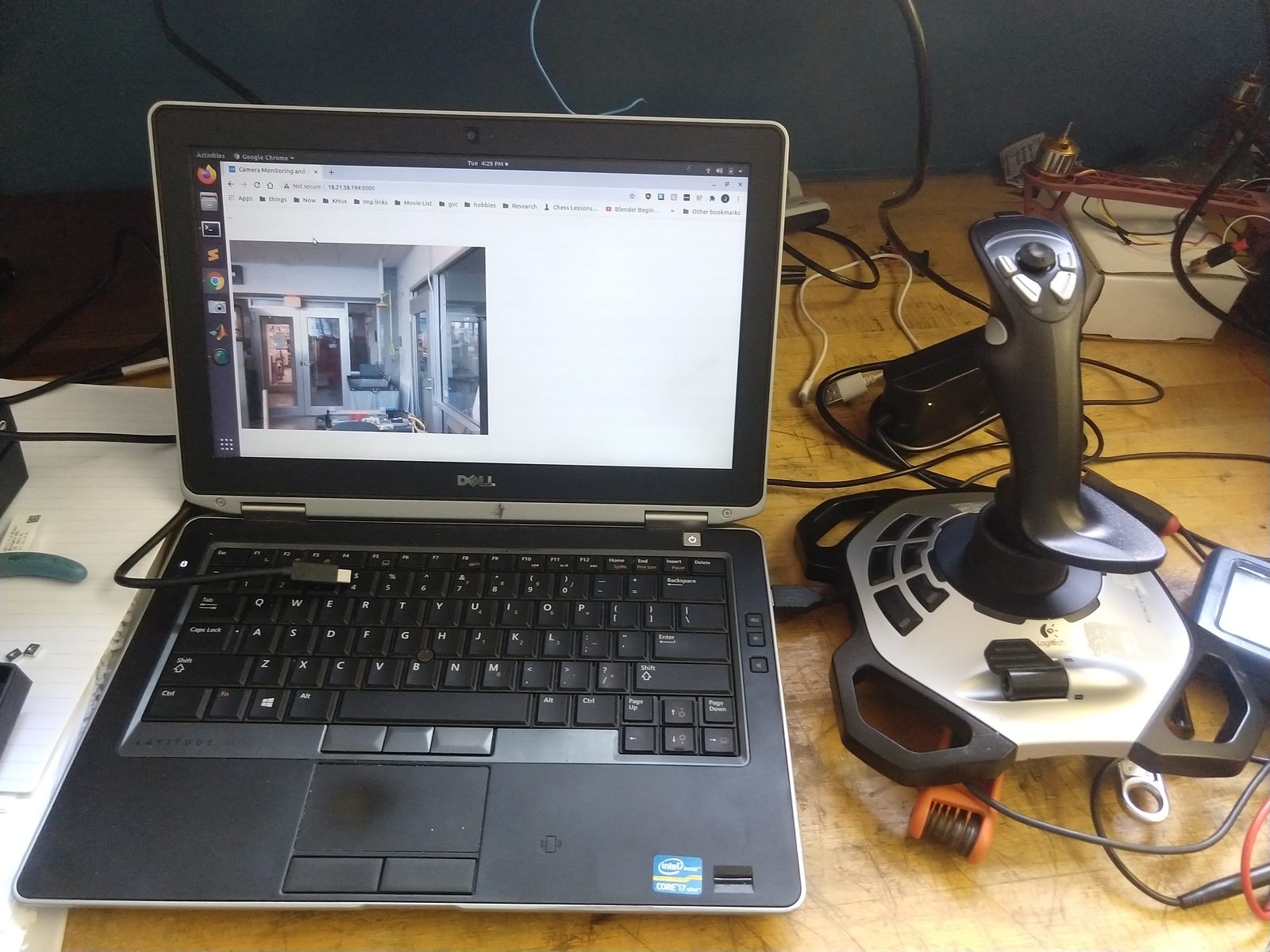 The teleoperation station: a laptop showing the robot's live camera feed in a browser served from the robot itself, with a Logitech joystick alongside it on the bench