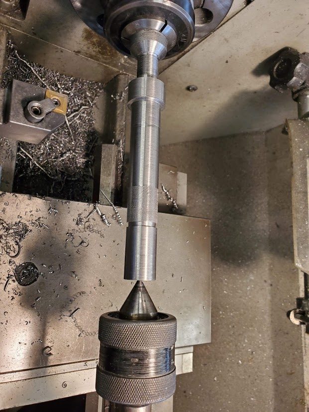 The steel spindle shaft held in the chuck and supported at the far end by a live centre in the tailstock, its knurled band and turned steps visible