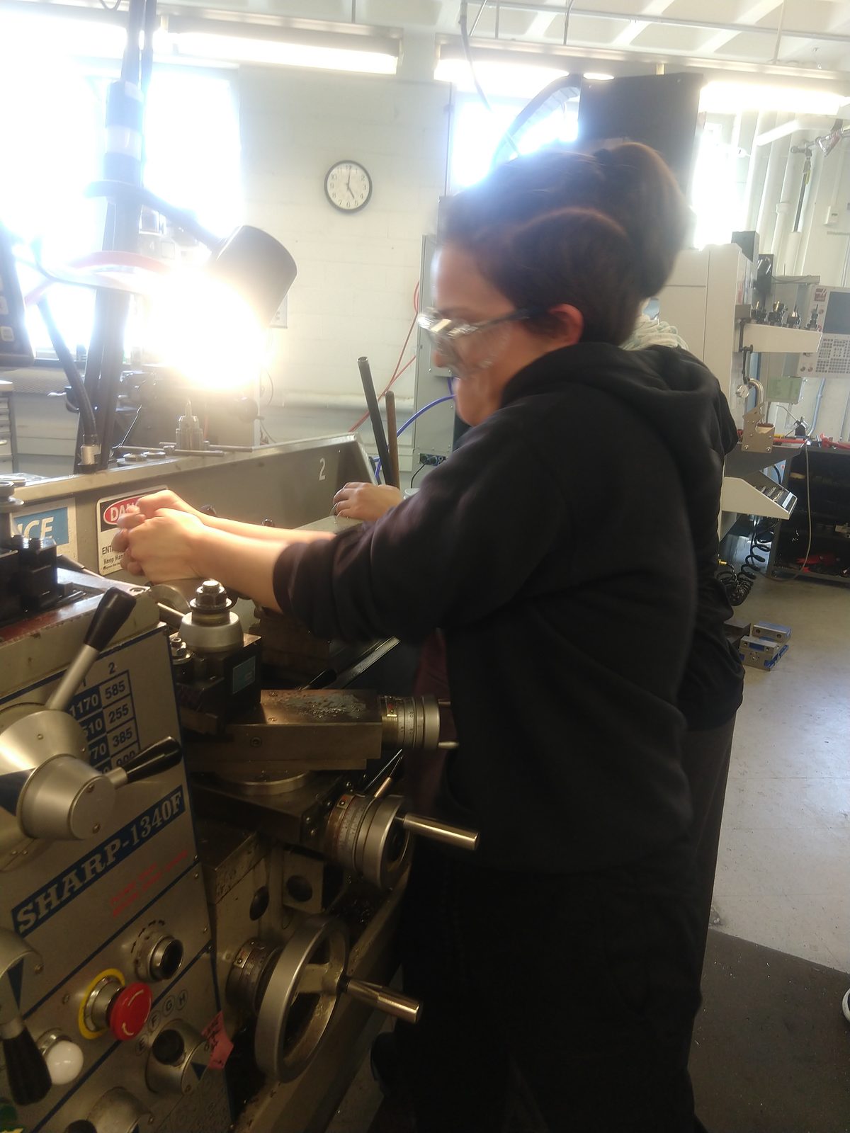 Me at a Sharp 1340F manual lathe in the MIT shop, safety glasses on, working the carriage handwheels while turning the spindle shaft