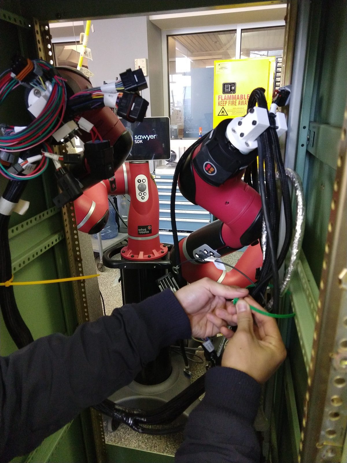 A worker zip-tying a harness held in place by the twin Sawyer arms inside the cabinet, seen over the arms