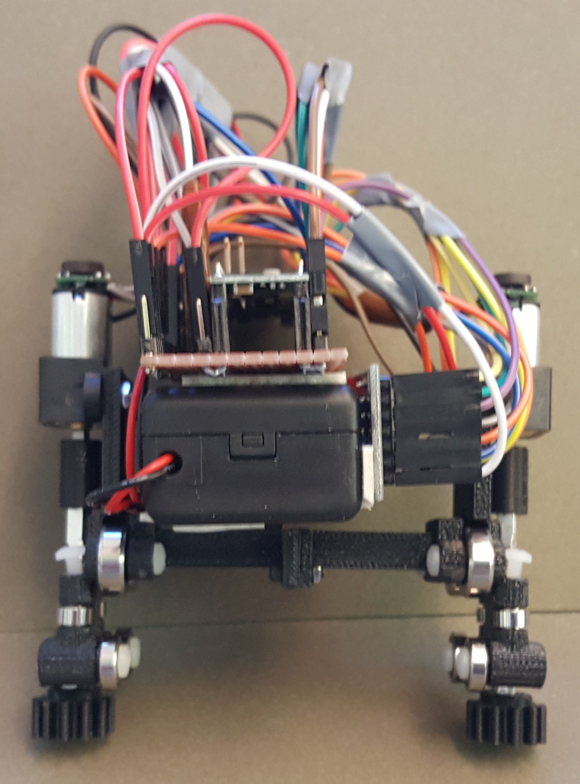 Photograph of the assembled carriage: a black 3D-printed chassis on four wheels with gear pinions, carrying a battery pack, control board and motors, with a bundle of coloured wires rising from it